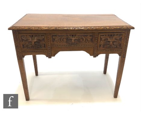 An early 20th Century oak side table or lowboy, fitted with three frieze drawers with carved Green Man mask handles, all abov