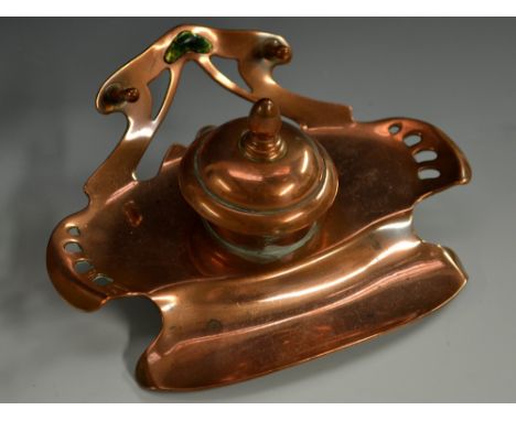 A Secessionist copper inkwell, hinged cover with knop finial, shaped and pierced back with enamel cartouche and pen rest, 16.