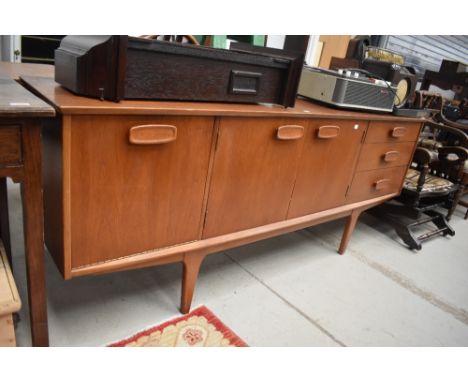 A vintage teak long john style sideboard having triple cupboard and three drawers, stylised legs and handles, circa 1970s