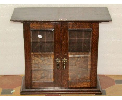 A small Edwardian/1920s oak wall or table cabinet, enclosed by a pair of bevelled edge rectangular glazed panelled doors, rev