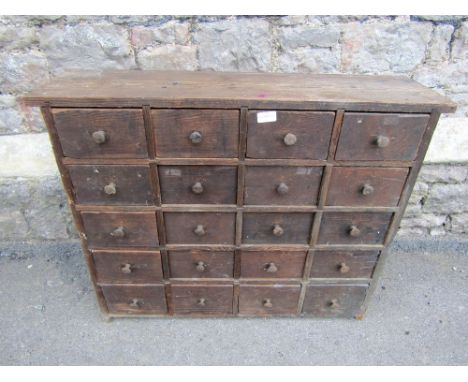 A vintage stained pine nest of twenty small drawers, with metal button knob handles, 86cm wide x 22cm deep x 70cm high