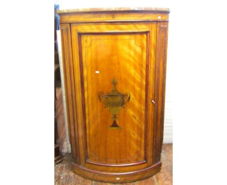 A Georgian floor standing satinwood veneered bow fronted corner cupboard, enclosed by a rectangular panelled door, with inlai