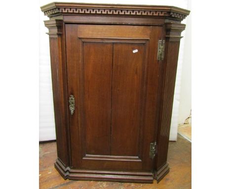 Georgian oak hanging corner cupboard, the panelled door flanked by fluted column supports and set beneath a Greek key frieze