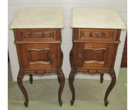 A pair of oak bedside cupboards of square cut form with white marble tops, each enclosed by a single door and frieze drawer w