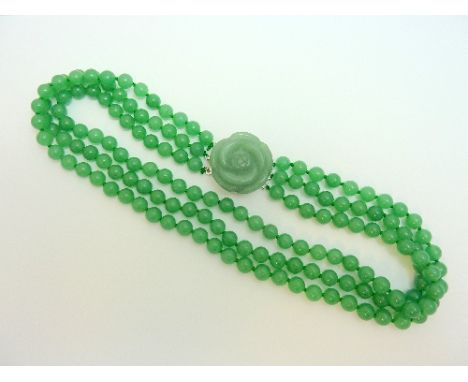 A JADE NECKLACE, comprising of three strands of jade beads to the carved jade flower clasp, length 48cm