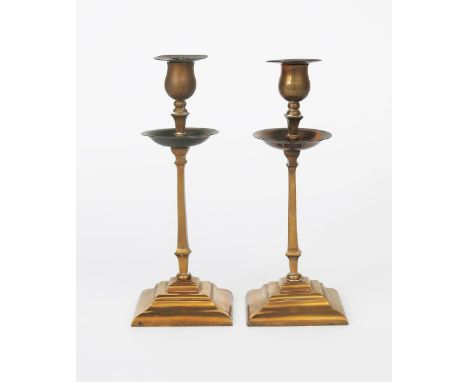 A pair of W.A.S. Benson patinated copper and brass candlesticks, model no.2A tapering square bases, on knopped square column 