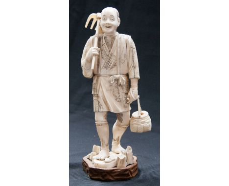 A Japanese okimono, Meiji, in the form of a farmer with fork and basket, on wooden stand, 25cm high