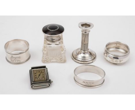An Art Deco period folding travelling timepiece: three silver serviette rings, a miniature silver pricket candlestick, and a 