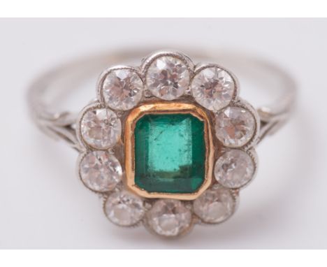 An emerald and diamond oval cluster ring:, the rectangular emerald within a surround of circular, old-cut diamonds estimated 