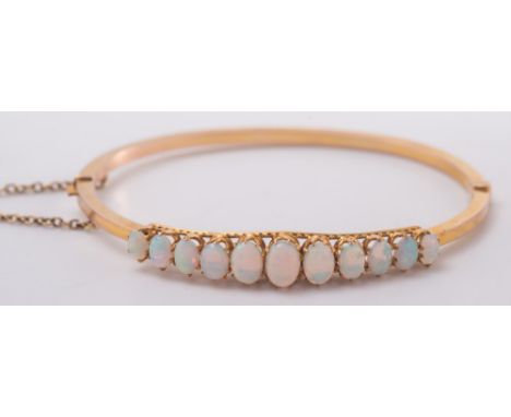 A gold and graduated opal hinged bangle: with safety chain. 