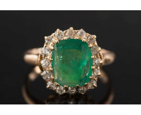 A gold, emerald and diamond cushion shaped cluster ring:, the cushion shaped emerald within a surround of circular, old-cut d