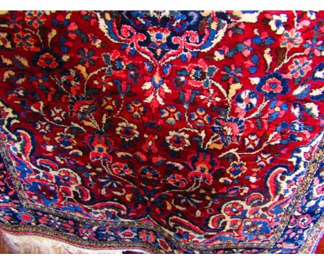 An eastern wool carpet with deep red field decorated with a central foliate medallion in shades of blue, pink, cream, etc, en