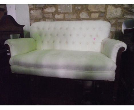 An Edwardian two seat sofa with cream ground floral patterned upholstered seat with rolled arms and button back raised on squ