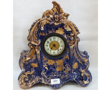 An early 20th century ceramic mantle timepiece, the rococo revival case gilded and blue glazed. 14' high