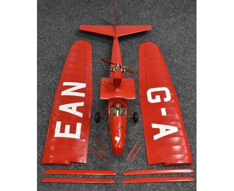 A Radio controlled model single wing Drone Airplane, red wings and fuselage, under wing bar connectors, rear facing petrol 0.