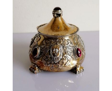 An Arts and Crafts silver pot and cover of circular tapering form, embossed with grotesque masks, ribbons and set with four o