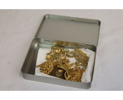 Tin containing nine vintage gold coloured Brooches, mostly numbered to the backs