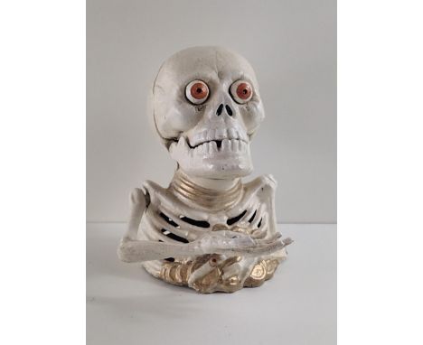 Cast metal money box in the form of a skeleton/skull, having pop-out eyes when coins inserted. Mechanical crank operation in 