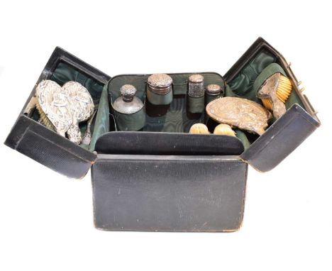 An early 20th century dressing table case, the black leather travel case with green silk lining, containing silver backed bru