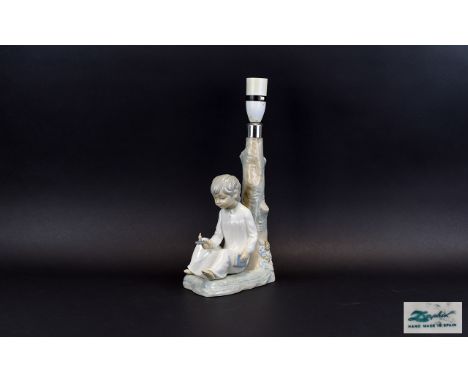 Lladro Lamp Base A charming lamp base in the form of a young boy in nightshirt holding a candle and book leaning against a tr