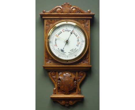Early 20th century oak case aneroid barometer, carved scrolls and floral spandrels, with centre coat of arms crest, circular 