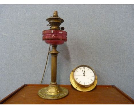An Art Nouveau brass and cranberry glass oil lamp (converted to electricity) and a Metamec quartz ship's style clock 