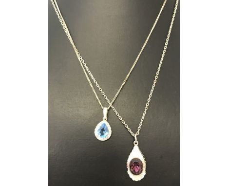 2 pendants on silver chains. One set with an amethyst and the other set with a blue topaz surrounded by small crystals. 