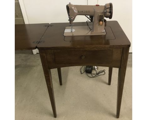 A 1960's dark wood 185k Singer electric sewing machine table with accessories, lamp and foot pedal. Table has central pull do