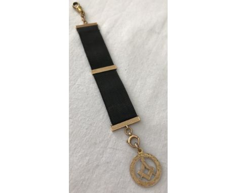 A 9ct gold Masonic fob mounted on a black ribbon clip. Ribbon has 15ct gold clasps and engine turned decoration. 