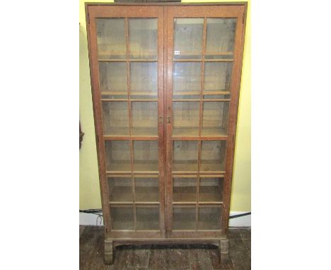A Cotswold School oak bookcase with exposed dovetail and through tenon jointed construction enclosed by a pair of full length