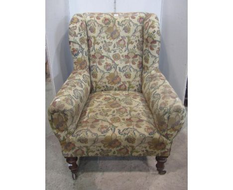 A Victorian drawing room chair with winged back, rolled arms, beige ground repeating floral patterned upholstery raised on tu