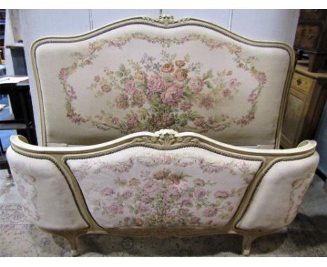 A French double bedstead with machine woven floral tapestry upholstered head and foot board with cream painted shaped carved 