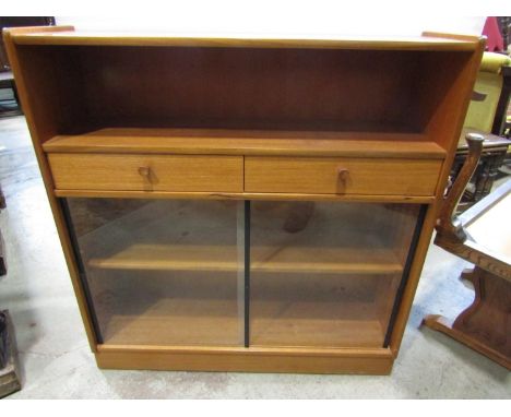 A retro teak floorstanding side cabinet/bookcase partially enclosed by sliding glass doors beneath two frieze drawers and ope