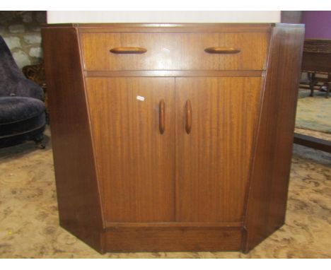 An E Gomme early G-plan floor-standing corner cupboard enclosed by a pair of doors beneath a secretaire drawer with brass pus