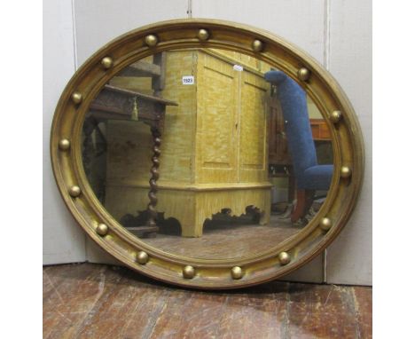 A Regency wall mirror of oval form with deep moulded gilt frame and ball surround,m 76 cm high x 92 cm wide 