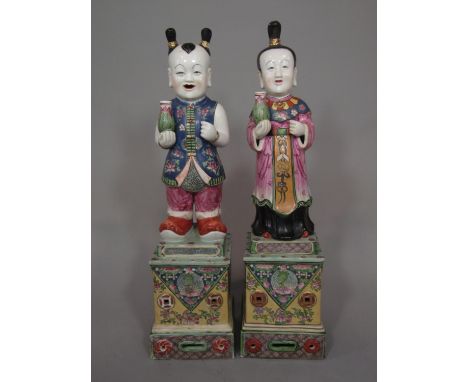 A pair of oriental polychrome figures of standing male and female characters, each holding a vase and raised on a square shap