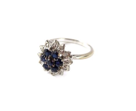 A sapphire and diamond cluster ring, set with seven dark blue sapphires, in claw setting, surrounded by twelve round brillian