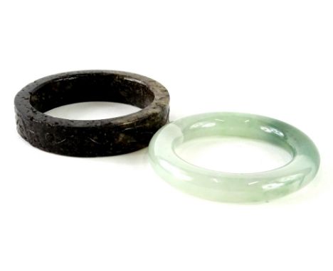 An oriental green hard stone bangle, and a carved soapstone bangle. (2)