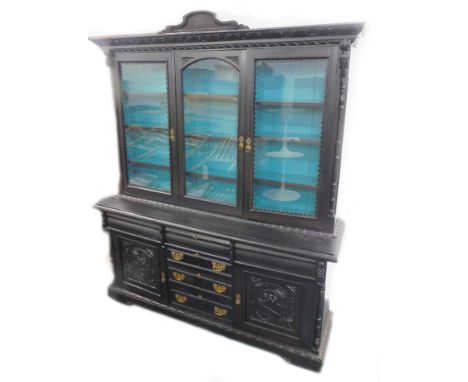 An ebonised oak sideboard, the top carved with scrolls, etc., above three glazed doors, flanked by turned pilasters, the base