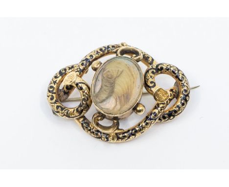 A Victorian yellow metal and enamel brooch, the centre with glazed compartment containing lock of hair mourning within a serp