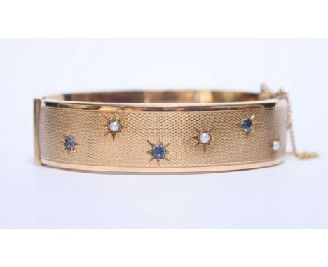 A 9ct gold stiff bangle, with engine turned decoration and inset with seed pearls and aquamarine coloured stones. 26.8 grams.