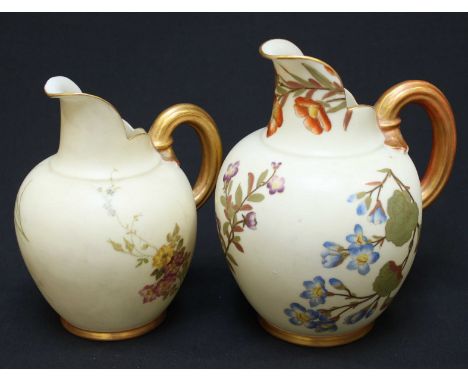 Two Royal Worcester ceramic jugs decorated with floral designs and gilded handles.