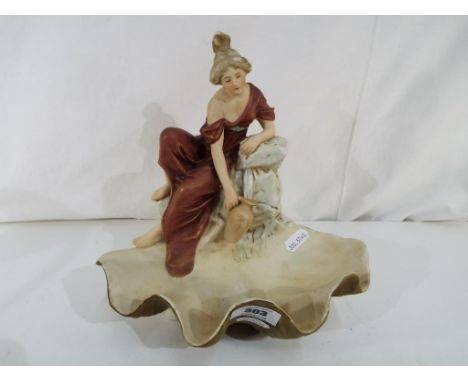Royal Dux - A ceramic centerpiece by Royal Dux of a classical female in a robe collecting water from a spring above a shell b
