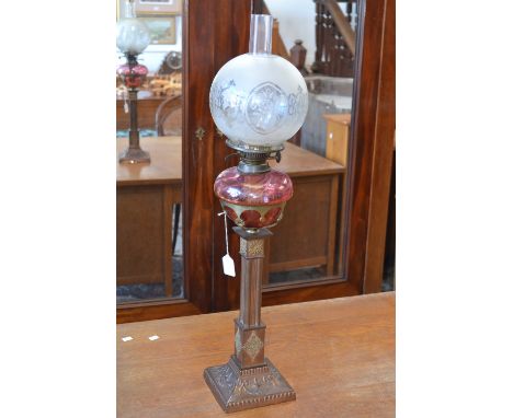 A Victorian oil lamp, etched glass globe, cranberry glass font, square column base and sloping socle, decorated with swags an