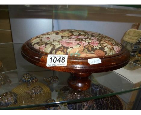 A Victorian footstool on bun feet with floral upholstery.