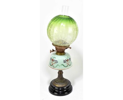 A Victorian oil lamp with green glass shade with floral decoration above the hand painted opaque glass reservoir on brass fla