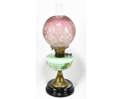 A Victorian oil lamp, the cranberry and clear shade with floral decoration above hand painted opaque reservoir on a brass fla