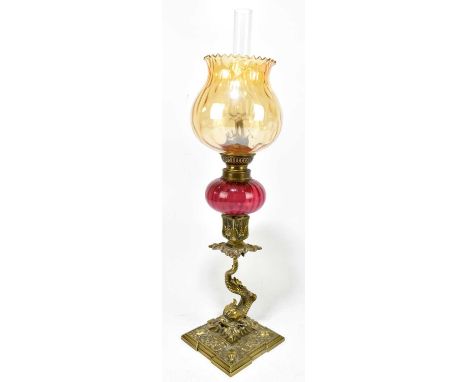 A 19th century gilt brass peg lamp, the amber coloured shade above a cranberry glass reservoir terminating on a mythical sea 