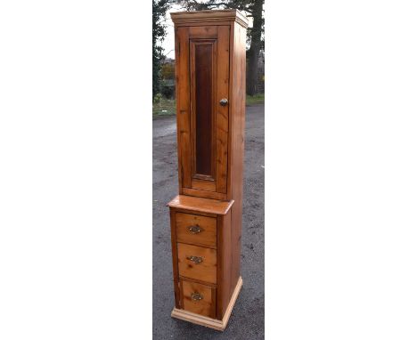 A pine narrow cabinet with panel door above three drawers, width 40cm, height 205cm.