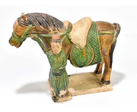 A Chinese Tang dynasty (218-906AD) Sancai glazed model of a horse with attendant standing to the side, on moulded rectangular